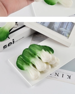 Realistic PVC green vegetable leaf keychain displayed on a white plate with books