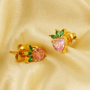 Detailed close-up of strawberry stud earrings with pink heart stones on gold satin fabric