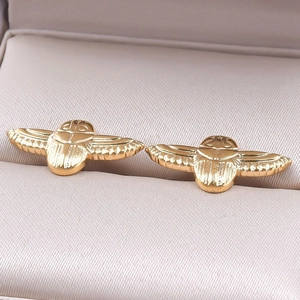 Macro shot of gold-plated scarab wing stud earrings in a soft pink jewelry box