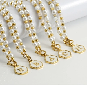 Détail du collier de perles avec fermoir OT et pendentif initial hexagone doré sur blanc