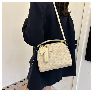 Detail of cream woven texture handbag with round handle and gold hardware on dark coat