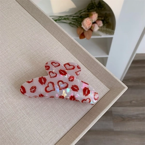 Detail of white acetate hair claw clip featuring red heart and lip prints on a tray