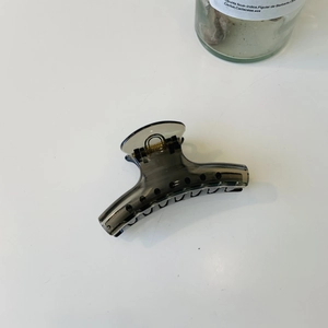 Detail of smoke grey translucent hair claw clip with golden spring on white surface