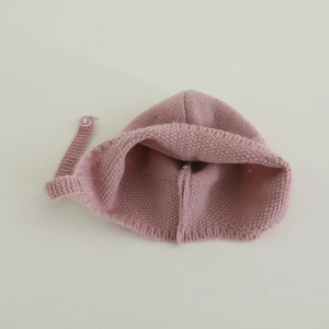 Dettaglio del cappello rosa a maglia per neonati con texture lana e chiusura a bottone