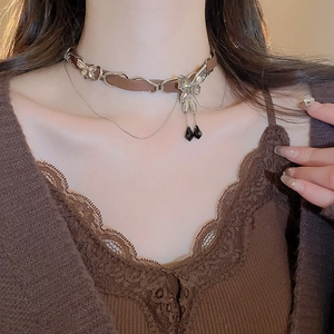 Detail of a brown leather choker featuring a silver bow and black teardrop pendants
