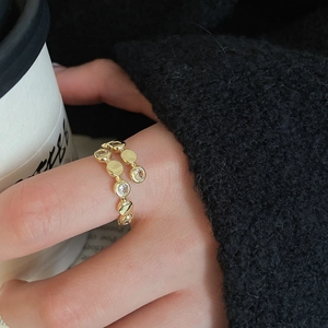 Close-up of golden triple-layer pearl and zircon ring worn on finger with elegant backdrop