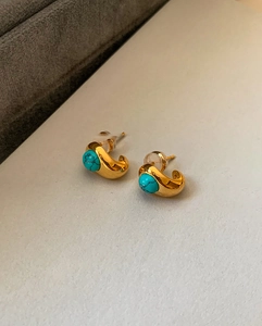 Detail of 18k gold plated C-shaped earrings with turquoise stones on a white background