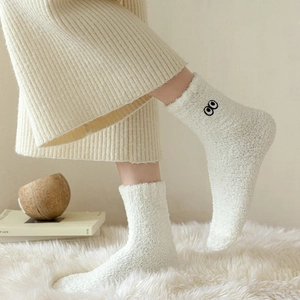 Close-up of white fleece socks with minimalist eye embroidery on a cozy carpet