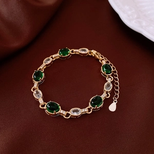 Detail view of gold bracelet featuring green oval stones and white zircon accents