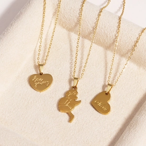 Three gold titanium necklaces with heart and Cupid pendants on a beige velvet display tray