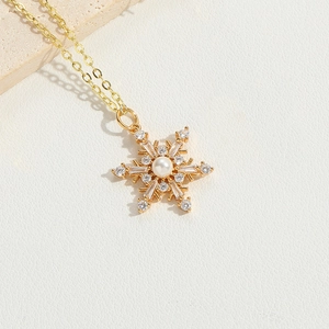 Elegant gold snowflake necklace with sparkling zircon and pearl pendant on white stone