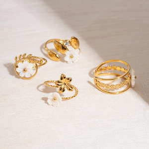 Set of four 18K gold plated rings featuring white flower designs on a beige textured surface