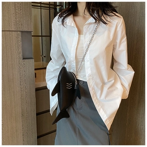 Close-up of a stylish black shark-shaped crossbody bag worn over a white shirt