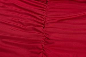 Detail view of red ruched knit fabric texture with central stitched wave pleats