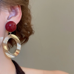 Close-up of model wearing brushed gold oval earrings with a dark red resin bead detail