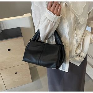 Side view of black lychee grain leather handbag held by model against a warm wooden background