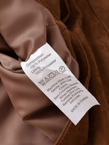 Detail of fabric care label on brown polyester jacket showing washing instructions