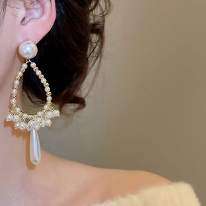 Detail of drop tassel pearl earrings with gold accents worn by a model in soft light