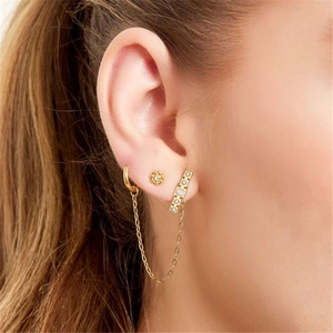 Detailed close-up of golden floral stud earring and chain link cuff with crystal accents