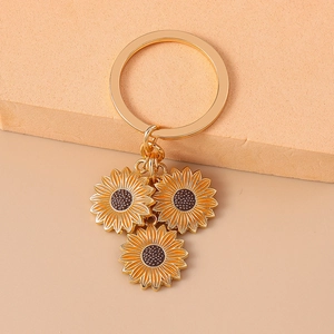 Pastel metal sunflower keychain with three yellow enamel pendants on a warm background
