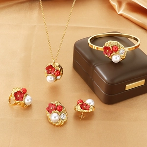 Detail view of gold jewelry set with red flowers and white pearls on satin background