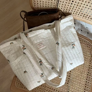 Detailed close-up of white quilted tote bag featuring fruit embroidery on woven fabric