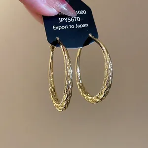 Golden woven texture hoop earrings with metallic spiral pattern held in hand