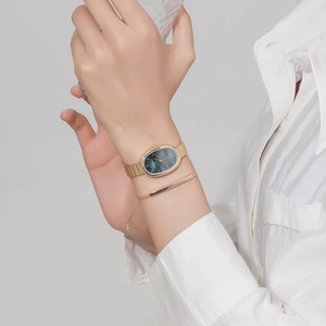 Detail of oval gold steel watch with green dial and matching minimalist bracelet