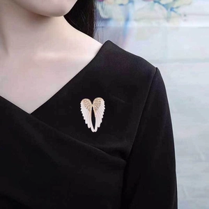 Close-up of angel wing brooch with crystals and white enamel on a black V-neck top