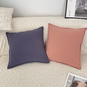Close-up of square cotton cushion covers in purple and coral orange on a cozy sofa