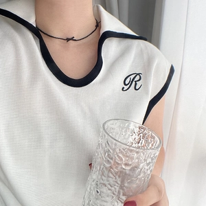 Detailed macro view of white waffle knit polo vest with black R letter embroidery and piping