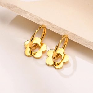 Golden stainless steel hoop earrings with hollow flower pendants on a textured surface