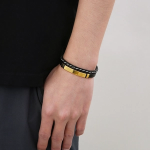 Detailed view of men's black braided leather bracelet with a polished gold metal tube
