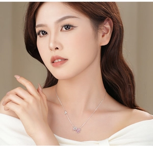 Macro detail of silver necklace featuring pink flower pendant and butterfly with zircons