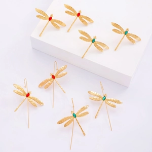Boucles d'oreilles libellule dorées avec pierres rouges et vertes sur socle blanc