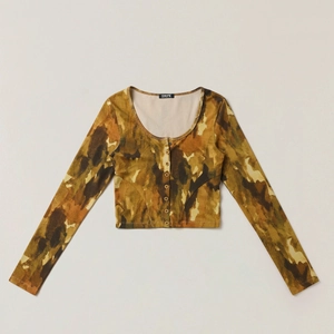 Dettaglio dello scollo a U e dell'etichetta SMFK sul cardigan corto in maglia mimetica