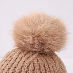 Close-up of thick knit winter hat with fluffy faux fur pompom in classic camel color