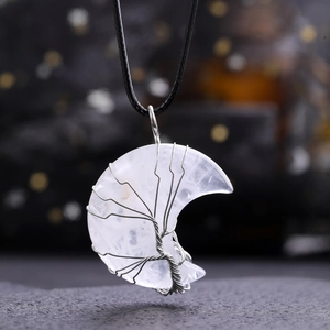 Macro shot of silver tree of life wire-wrapped crescent moon crystal pendant on black cord
