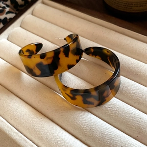 Close-up of tortoise shell resin C-shaped hoop earrings on a beige velvet jewelry box
