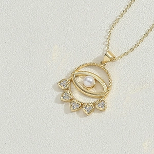 Close-up of 14K gold plated necklace with devil's eye pearl and heart zircon charms
