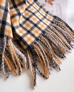 Detailed view of orange and black plaid scarf texture with soft tassel fringe detail