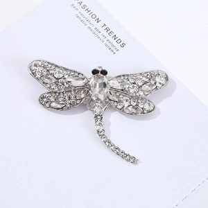 Detailed close-up of a silver dragonfly brooch with sparkling crystals on a magazine page