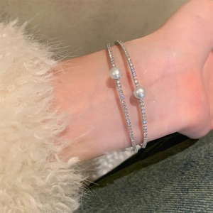 Detail of two silver bangles with micro-pave diamonds and central pearls on wrist