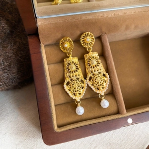 Detailed view of hollow geometric gold earrings with pearls in a wooden jewelry box