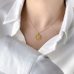 Close-up of golden sun pendant necklace on model wearing white satin shirt