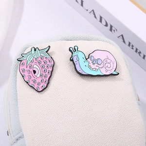 Close-up of pink strawberry with eyes and skull snail enamel pins on a canvas bag