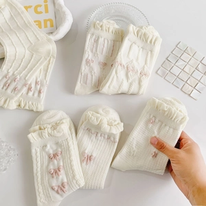 Detailed view of white cotton socks featuring pink bow jacquard and ruffle trim edges