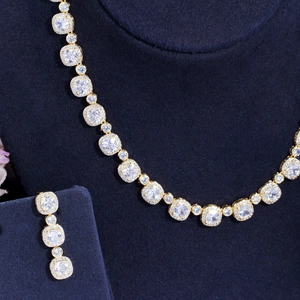 Detailed view of gold necklace and earring set with square zircons on blue velvet