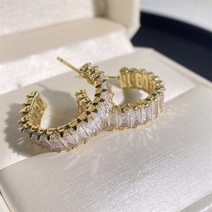 Boucles d'oreilles dorées en C avec zircons carrés dans une boîte en soie blanche