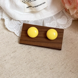 Detail view of round yellow acrylic geometric earrings on a wooden base with lace
